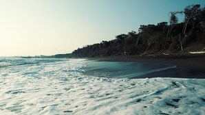 Ein Strand mit weißem Sand und Fußabdrücken, ein klarer Himmel und eine entfernte Küstenlinie mit Bäumen.