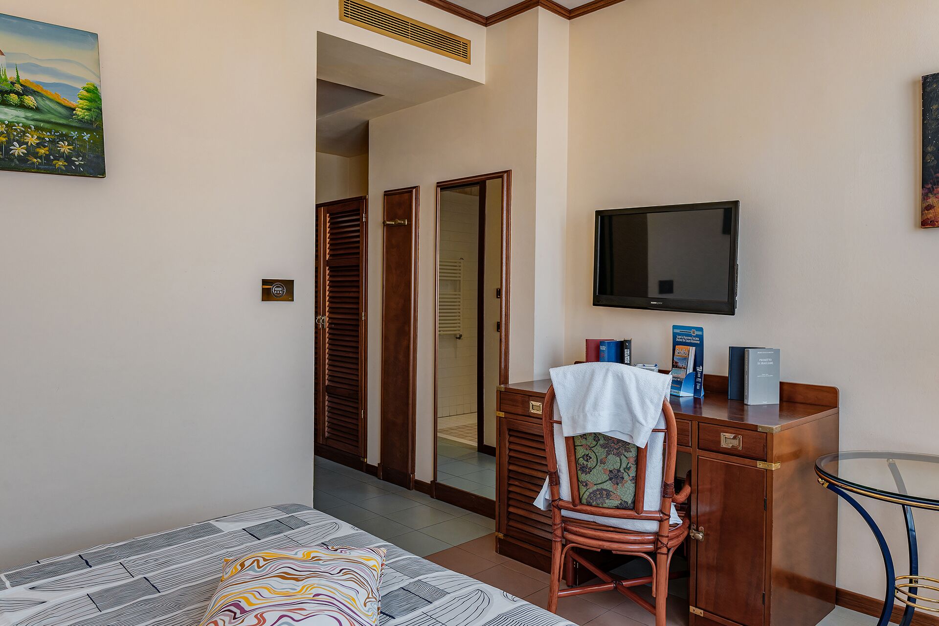 A hotel room with a bed, a desk with a chair, a television, and a wardrobe.