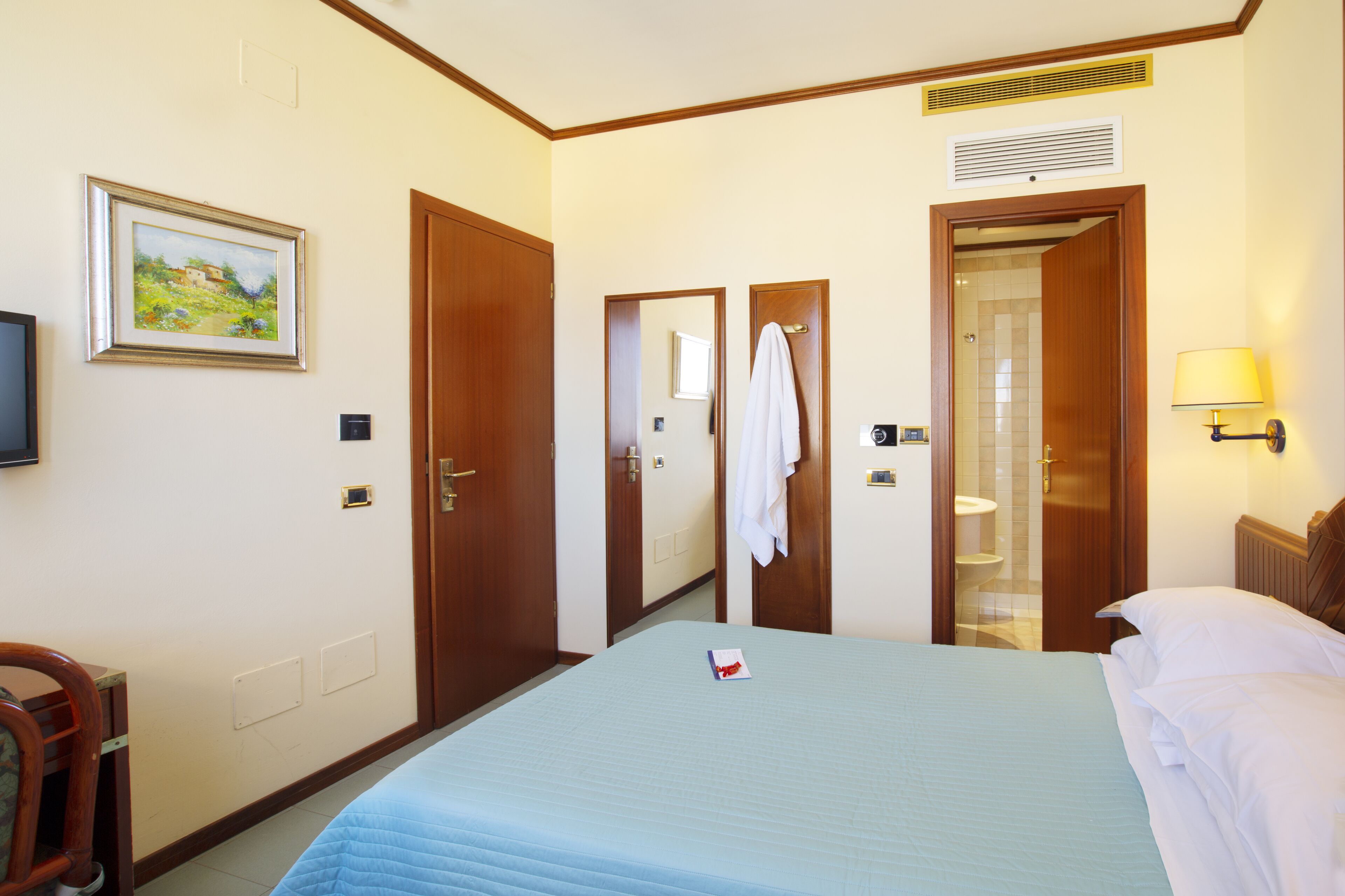 Une chambre d’hôtel avec un lit, une télévision, un tableau et une salle de bain visible à travers une porte ouverte.