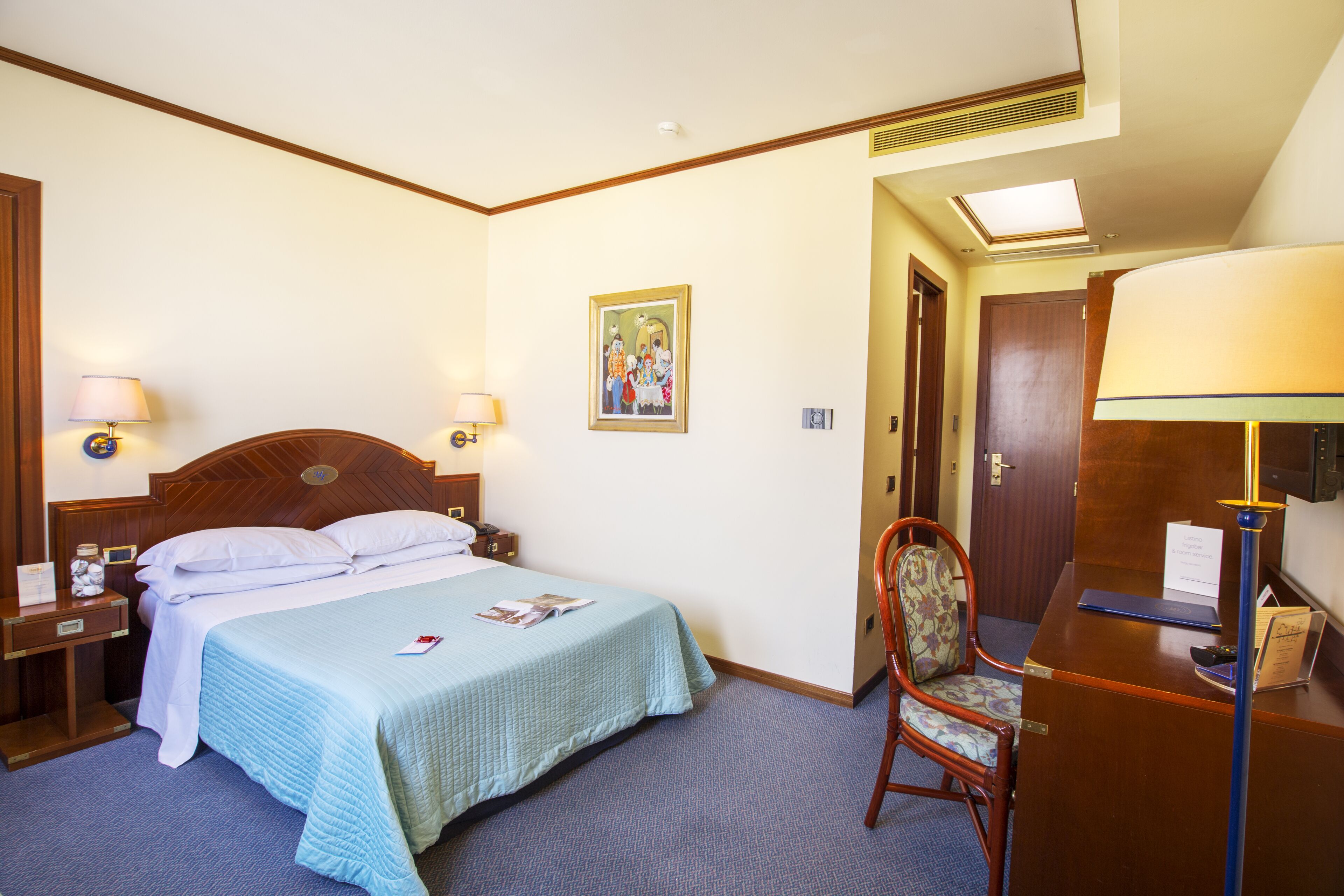 A hotel room with a bed, a desk, a chair, and a nightstand.