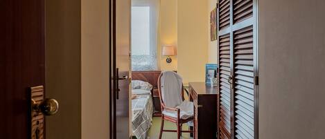Habitación de hotel con cama, una silla, escritorio y ventana con persianas.