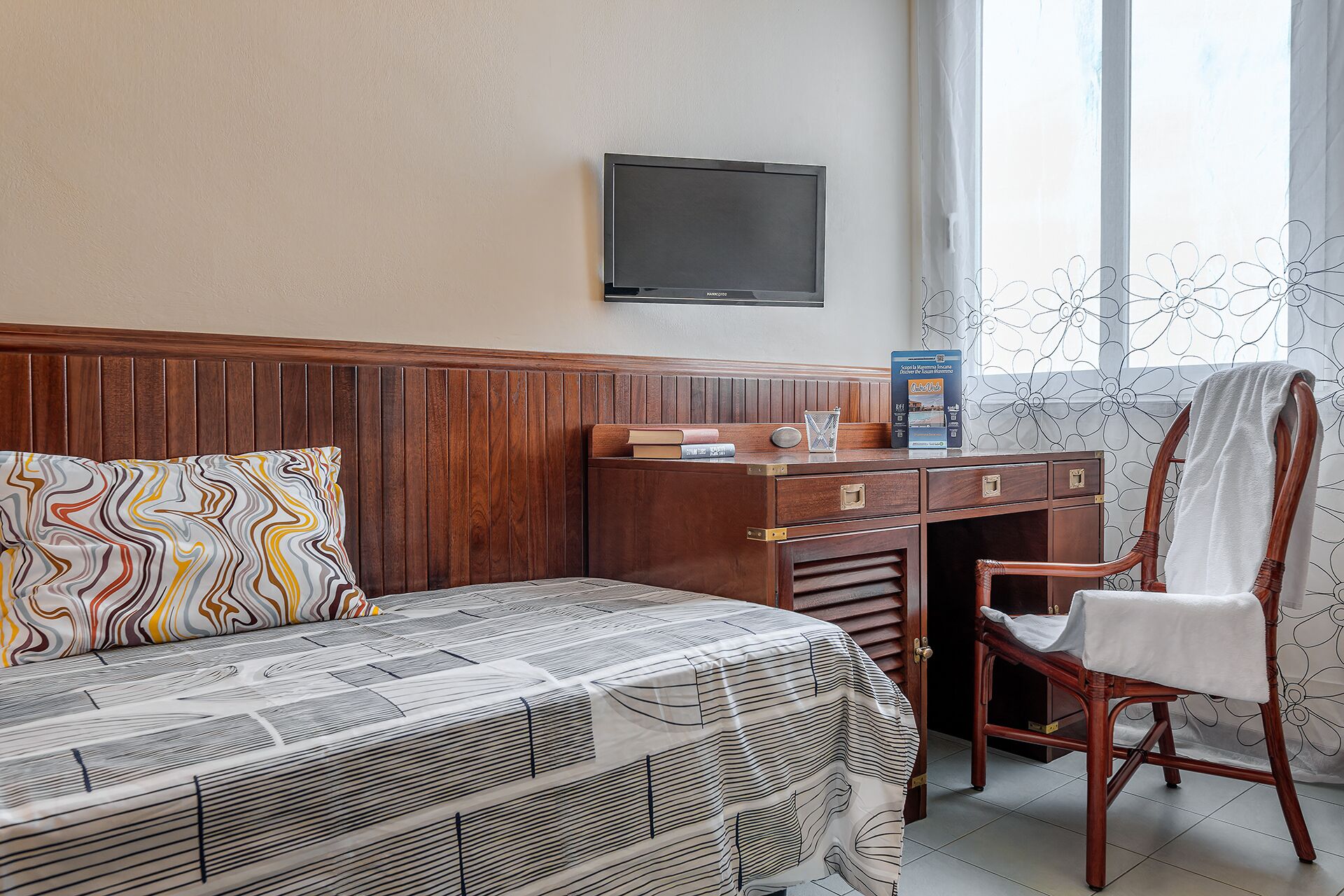 Una habitación de hotel con una cama, un escritorio, una silla y un televisor en la pared.