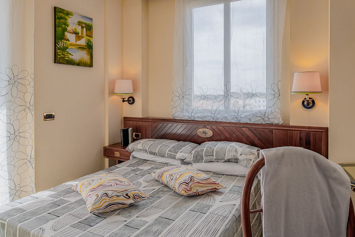 Una cama bien hecha con ropa de cama estampada, cabecera de madera y dos lámparas de noche.
