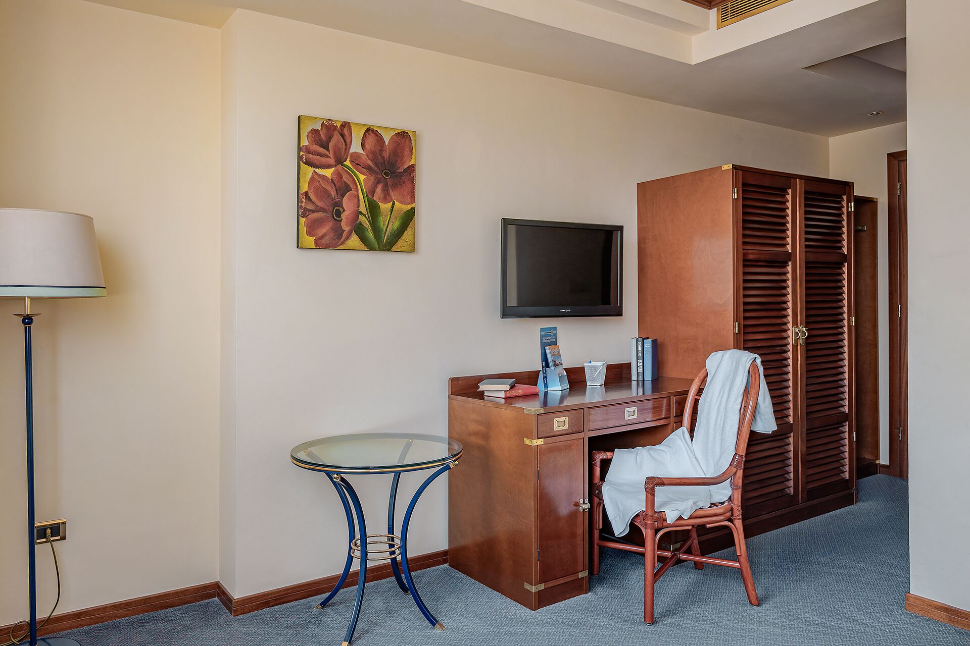 A hotel room with a desk, chair, television, and a wardrobe.