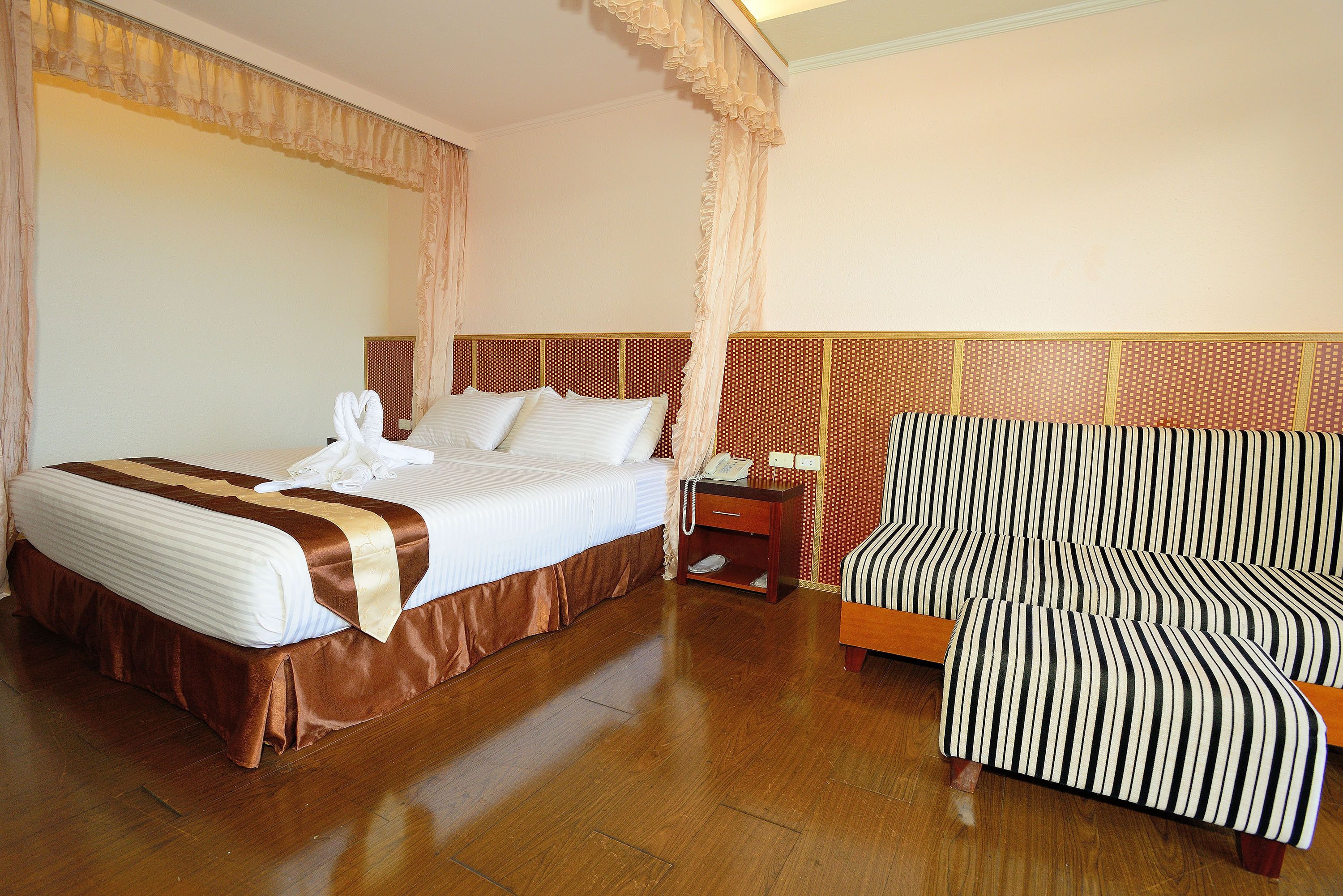 A hotel room with a large bed, a bedside table with a lamp, and a striped armchair.