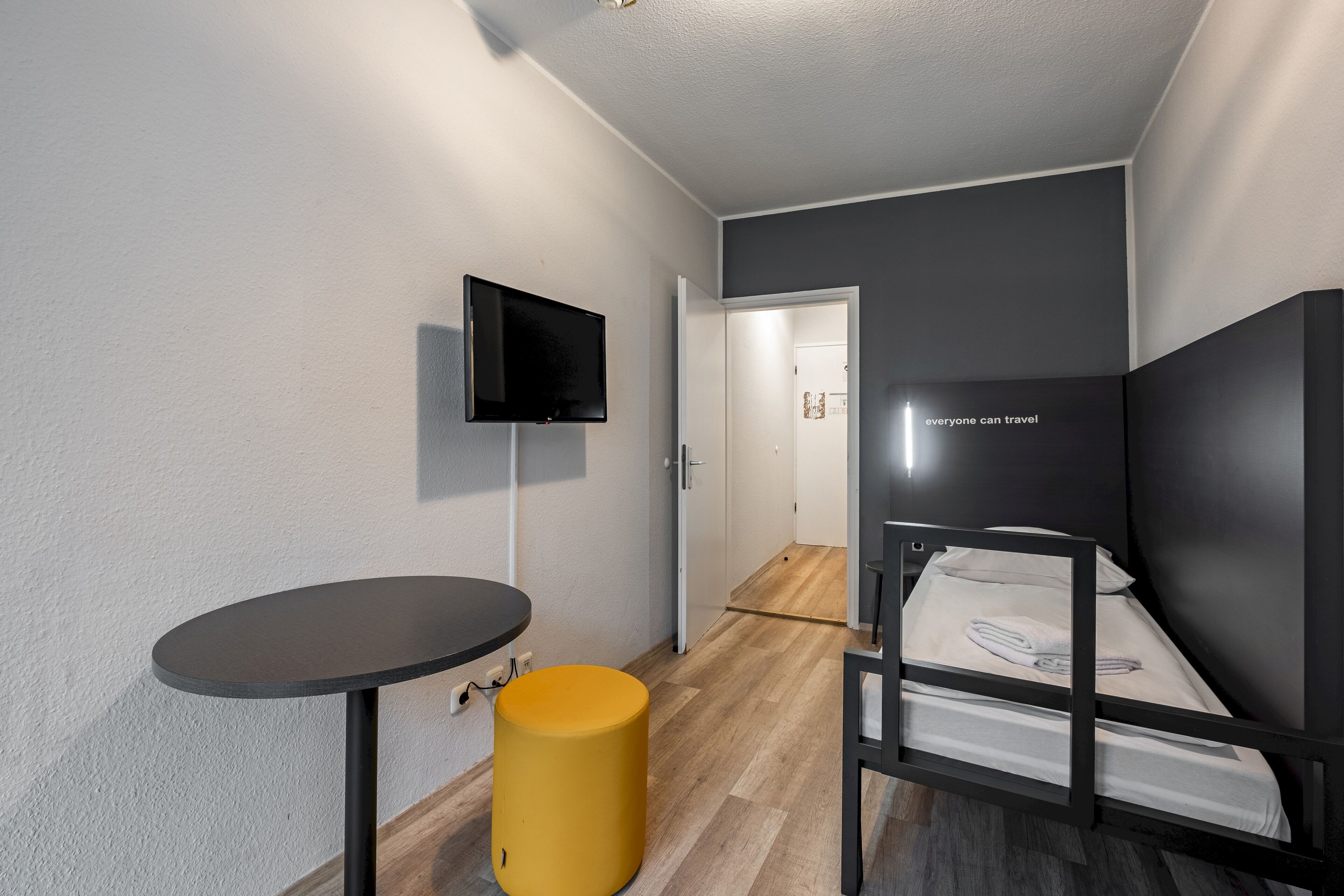 A compact room with a bed, a small table, a television, and a door leading to another room.