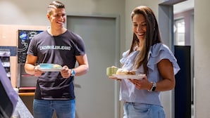 Two people holding plates with food in a room with a clock and a sign on the wall.