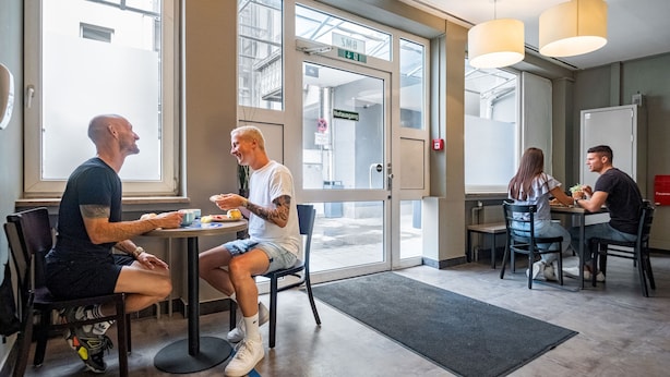 A modern indoor dining area with large windows, a door marked "SMB," and a visible exit sign.