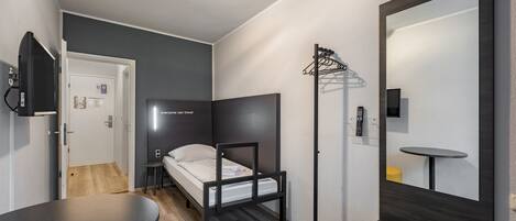 A compact room with a bed, a small table, a mirror, and a TV.
