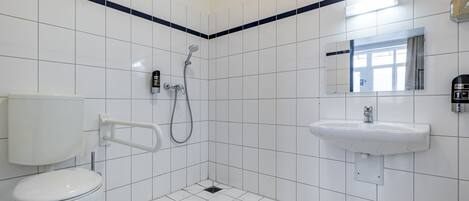 A bathroom with white tiles, a toilet, a shower, and a sink.