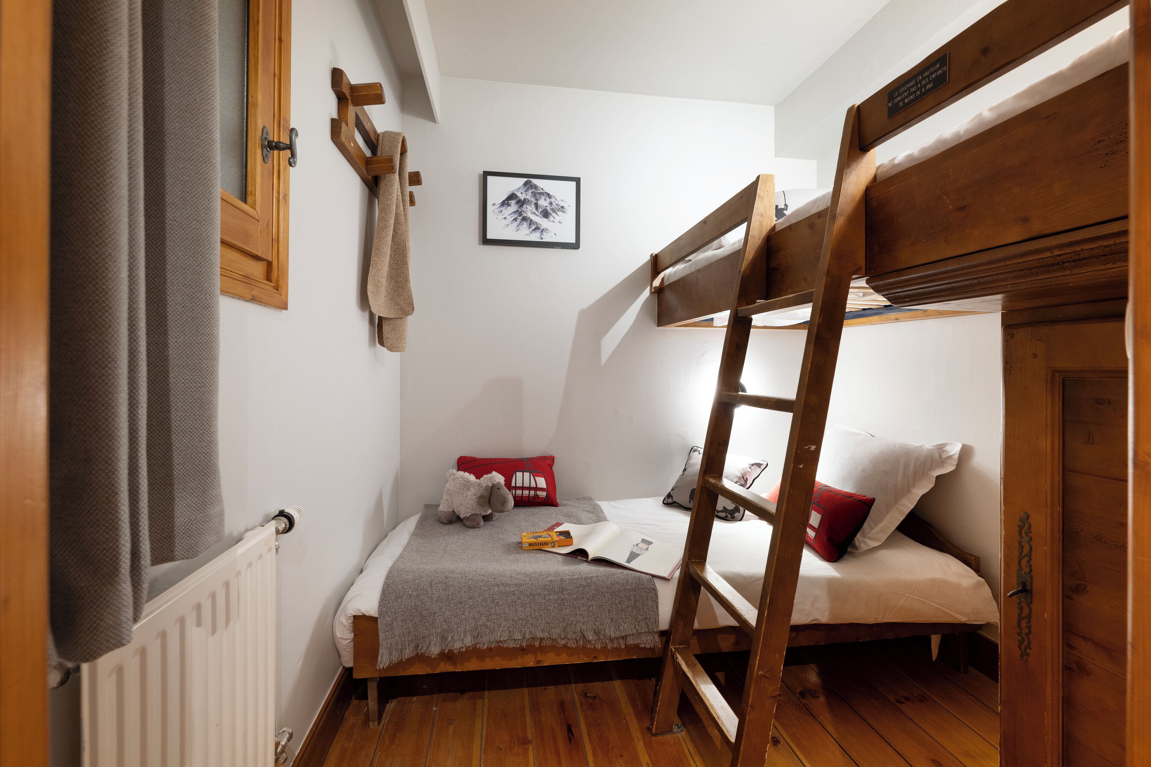 A compact bedroom with a bunk bed, a small bedside table, a radiator, and a framed picture on the wall.