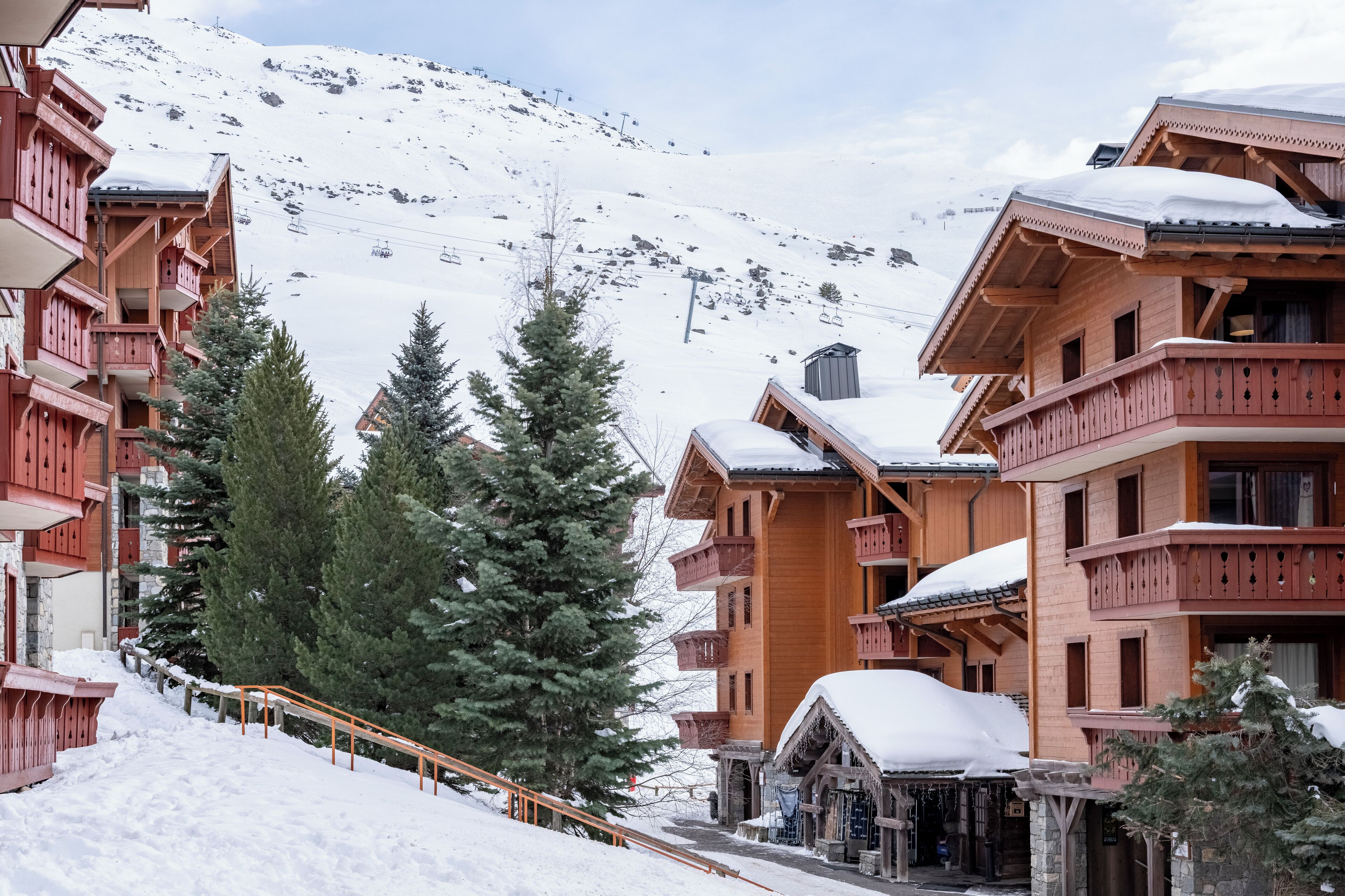 A wooden chalet-style building with balconies and a snow-covered mountain in the background.