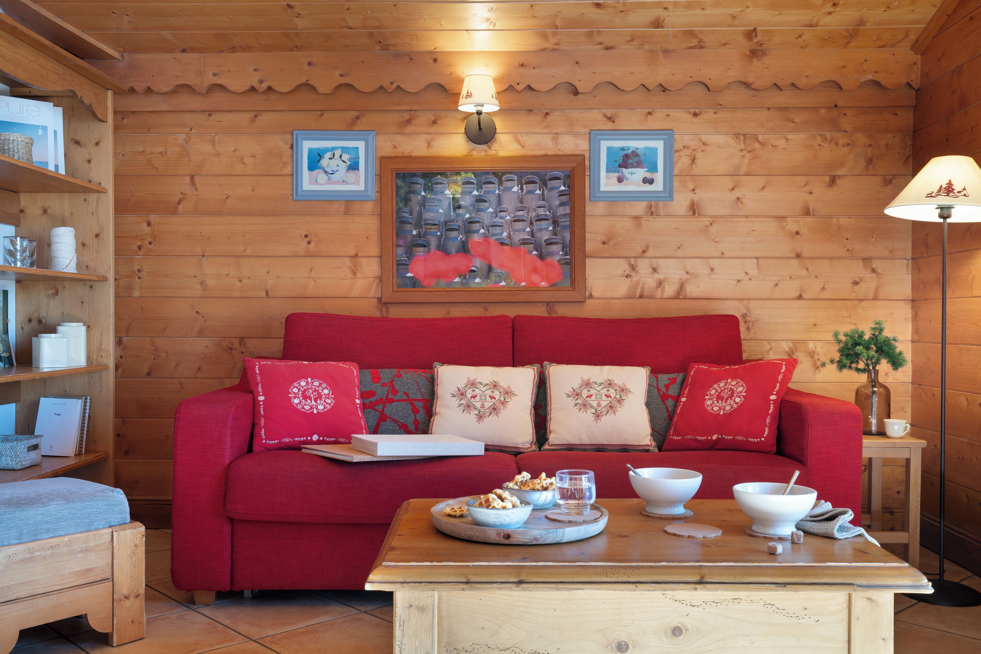 Ein gemütlicher Raum mit Holzvertäfelung, ein rotes Sofa mit dekorativen Kissen, ein Holztisch mit Schüsseln und Gläsern und eine Wandlampe.