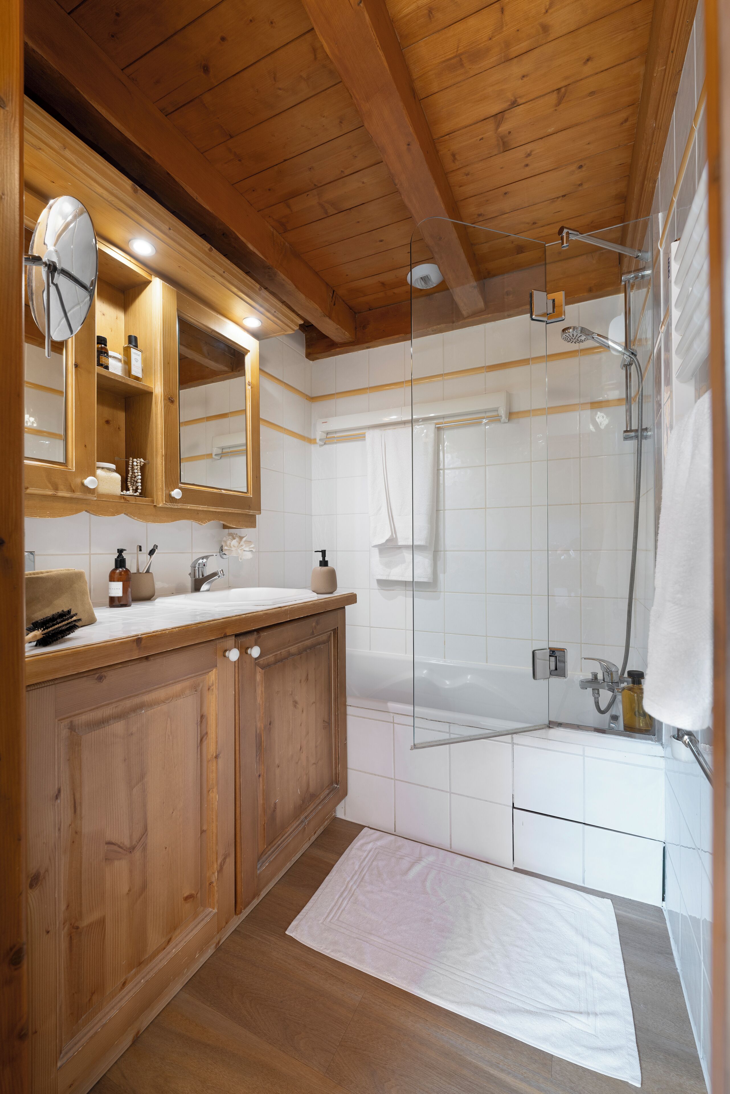 A wooden ceiling, a glass shower enclosure, a white bathtub, and a wooden vanity with a mirror.