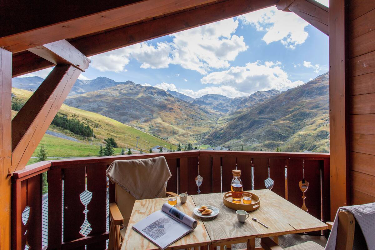 Eine Holzterrasse mit gedecktem Tisch, mit Blick auf eine Berglandschaft.