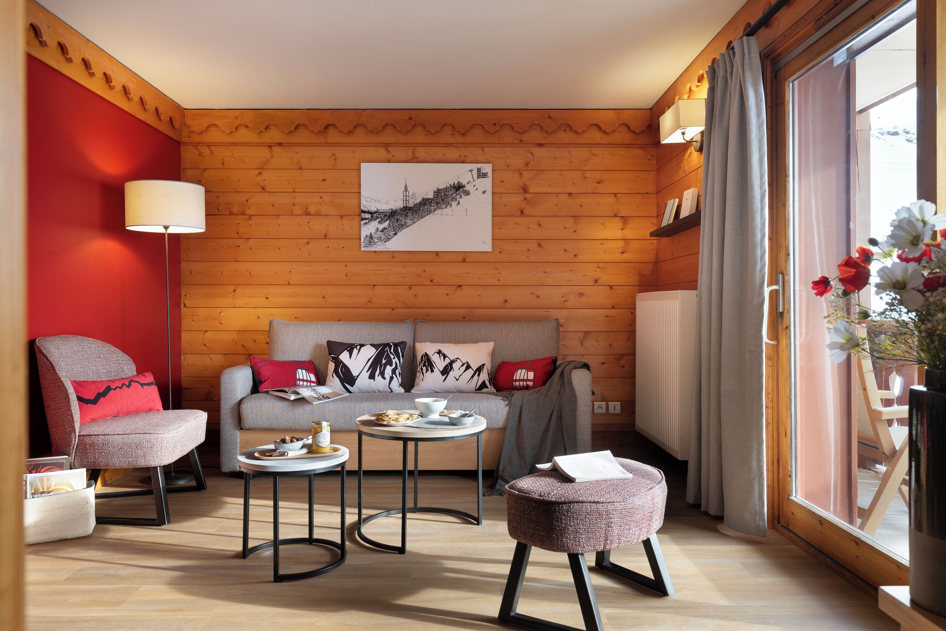 Una habitación acogedora con pared de madera, un sofá con cojines, una mesita con lámpara y una ventana con flores.
