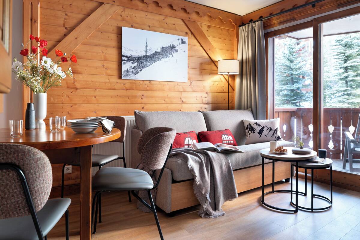Ein gemütliches Wohnzimmer mit Holzwand, einer Couch, einem Couchtisch und einem Essbereich mit Stühlen und einem Tisch.