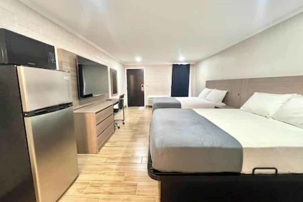 Moderni hotellihuone, jossa on pieni keittiö, kaksi sänkyä ja televisio.