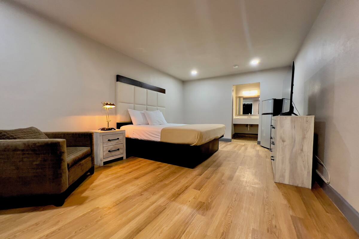 A modern bedroom with a bed, bedside table, lamp, and a small seating area.