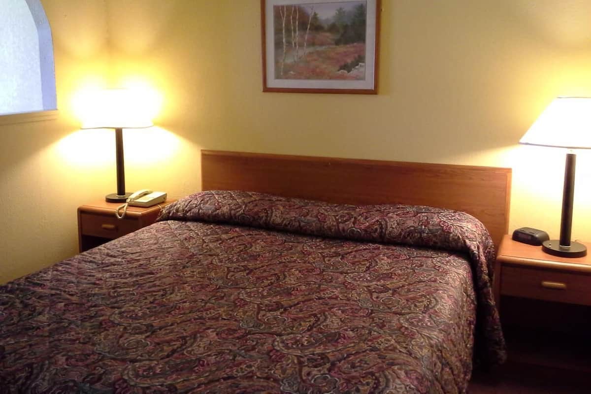 A hotel room with a bed, two bedside lamps, a nightstand with a phone, and a framed picture on the wall.