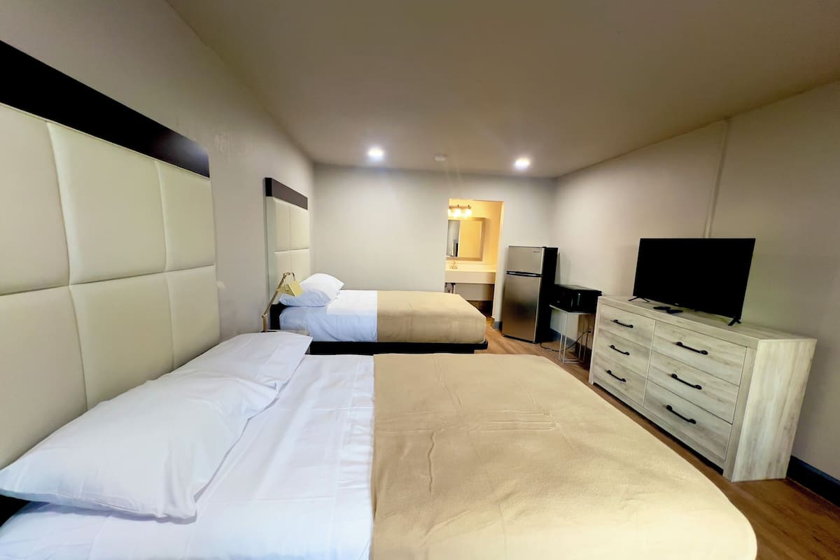 A hotel room with two beds, a TV, a refrigerator, and a dresser.