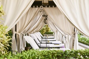 A row of lounge chairs under a canopy with a view of greenery.