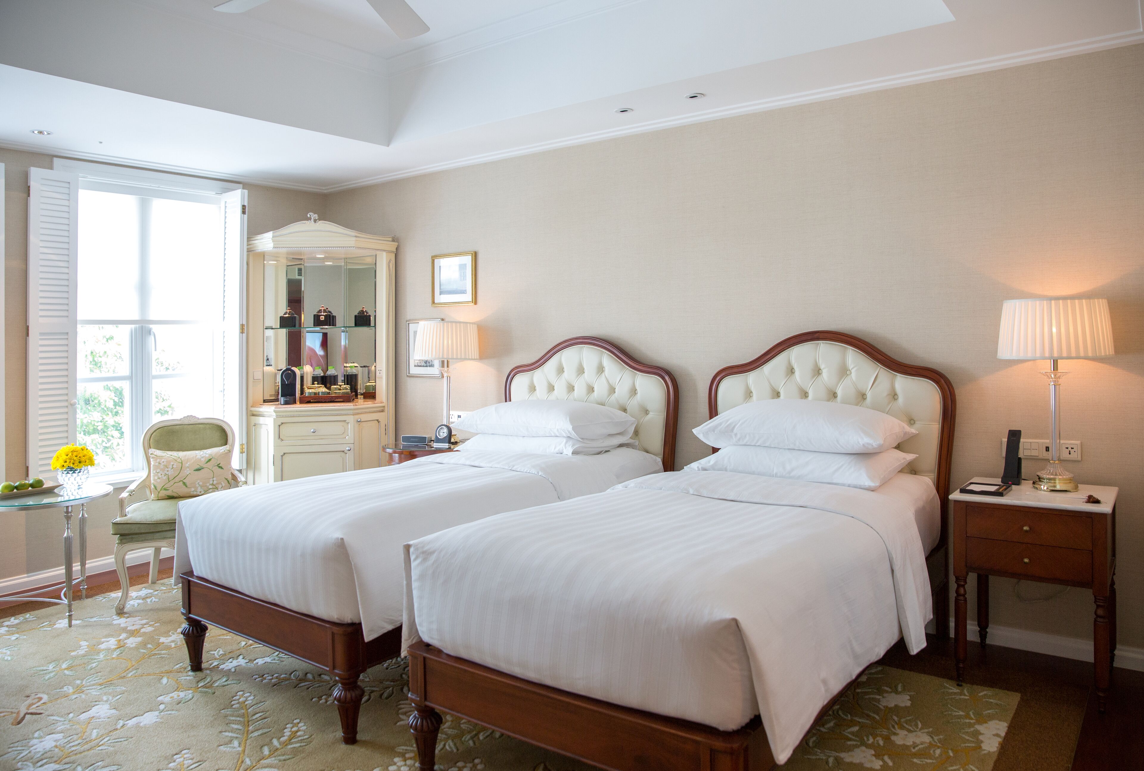 A hotel room with two beds, a vanity with a mirror, a chair, and a small table with a lamp.