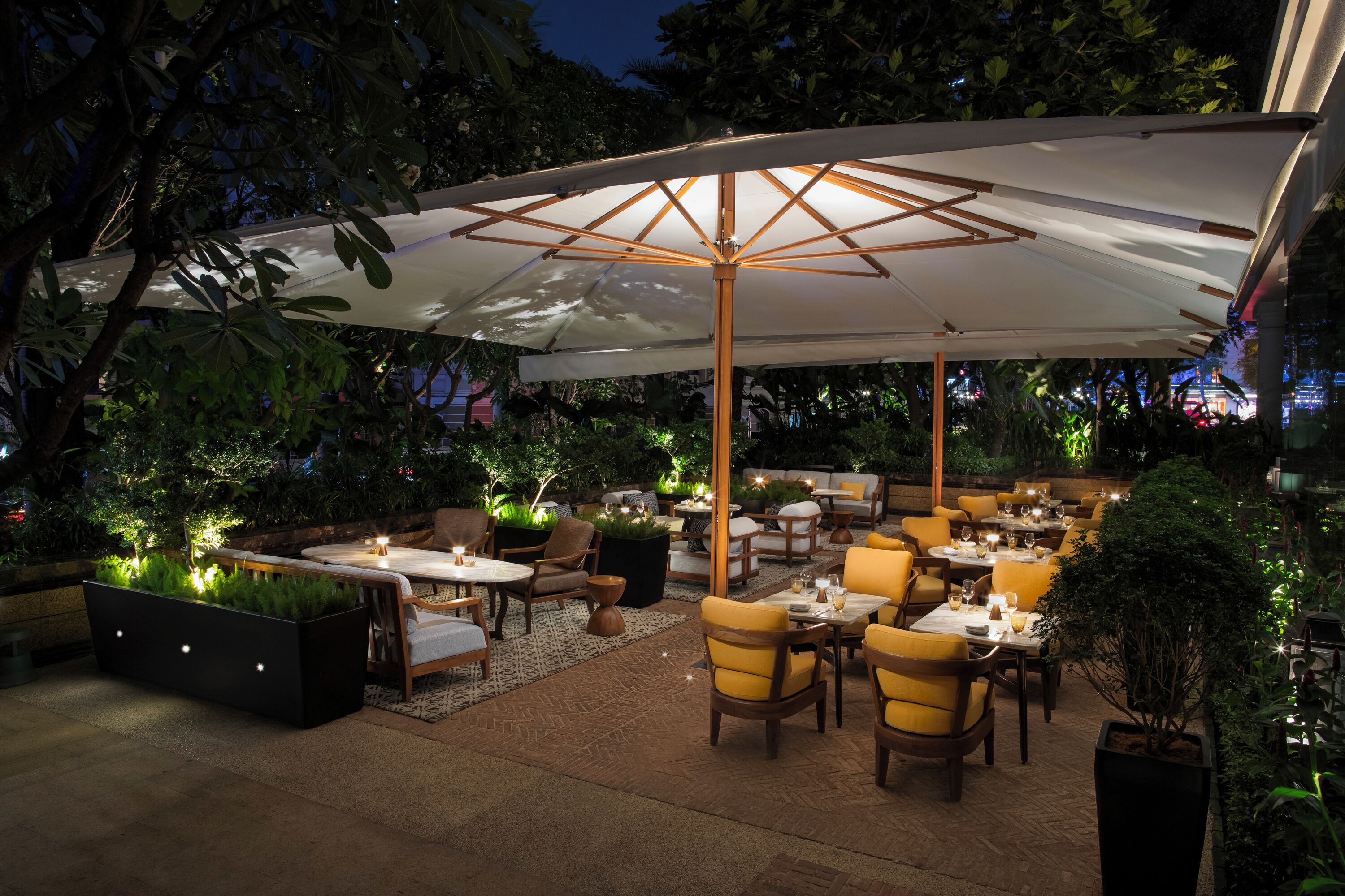 An outdoor patio area with tables and chairs, a large umbrella, and potted plants.