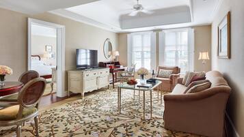 A spacious living room with a large window, a ceiling fan, a flat-screen TV, a sofa, a coffee table, and a decorative rug.