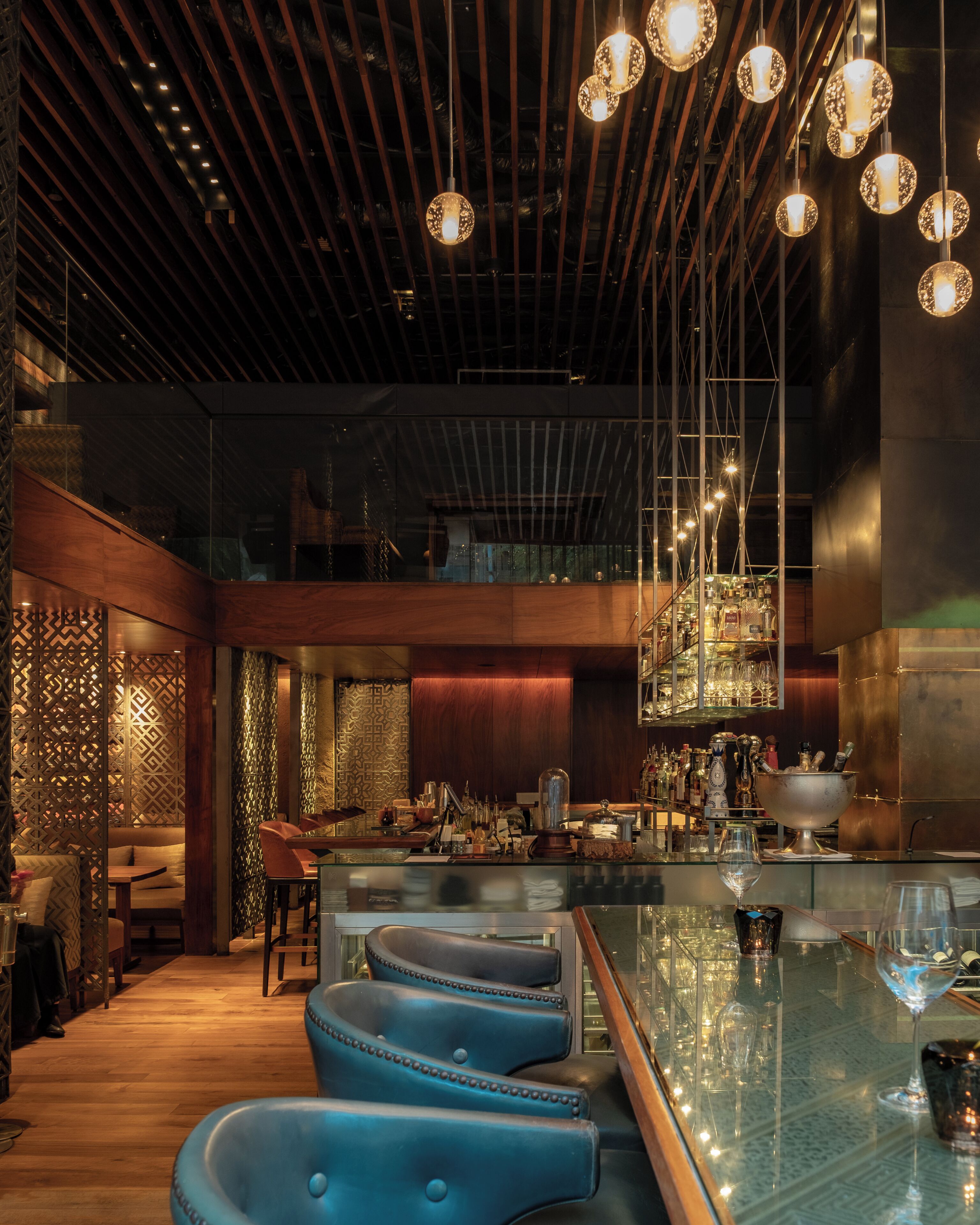 A modern bar area with a glass countertop, stools, and a variety of bottles.