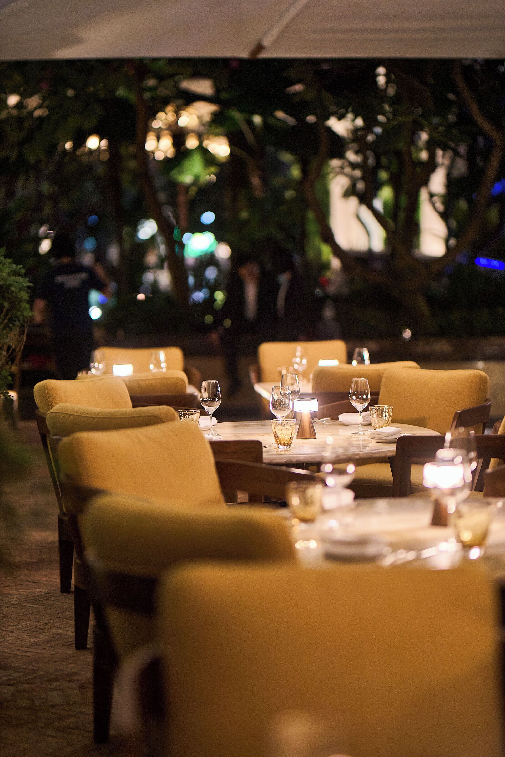 An outdoor dining area with tables set for two, surrounded by chairs.