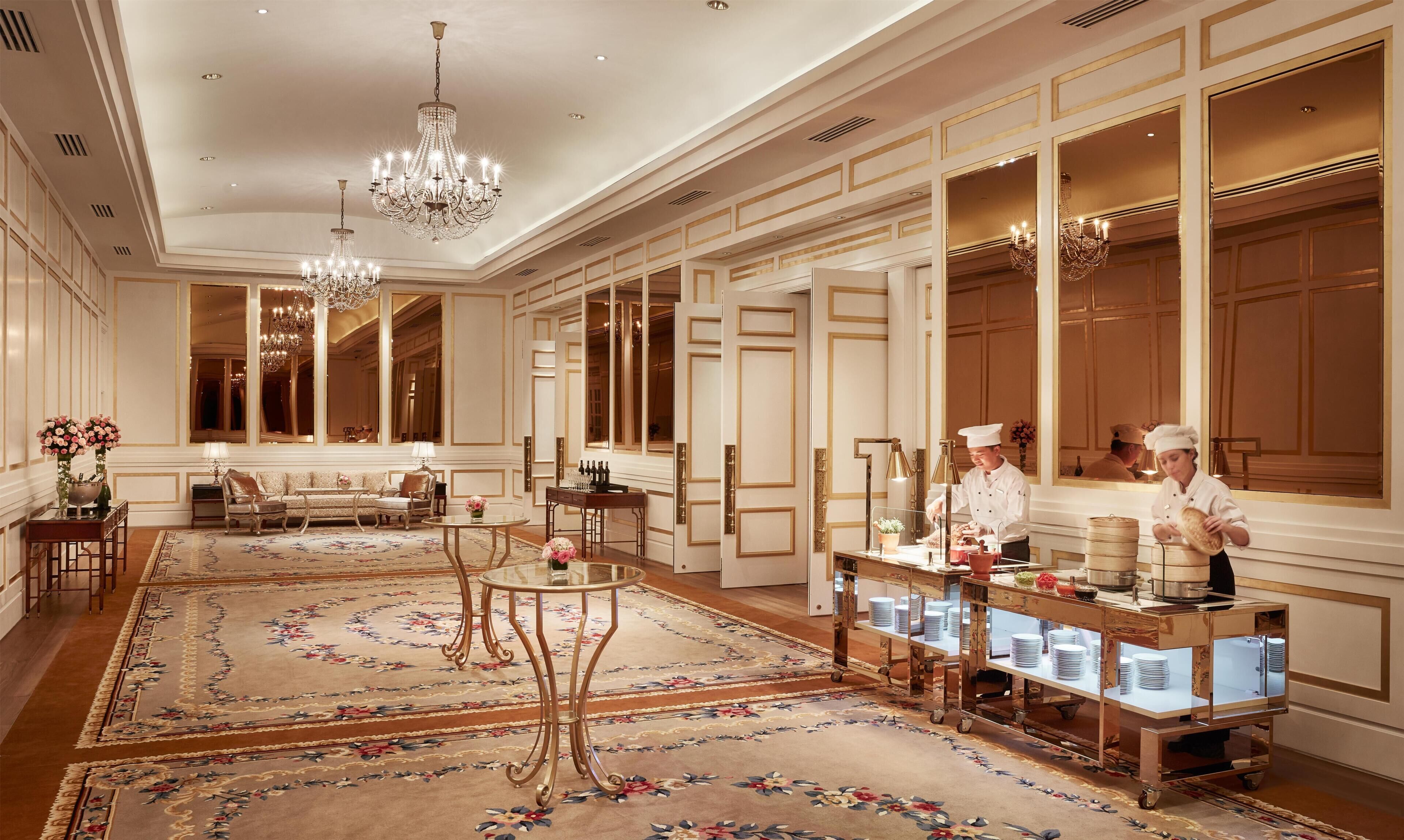A luxurious hotel lobby with chandeliers, a seating area, and a buffet setup.