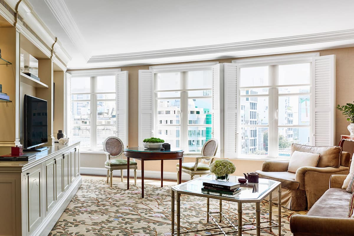 Une chambre d’hôtel comprenant un lit, une télévision, un bureau avec une chaise, un canapé et de grandes fenêtres donnant sur la ville.