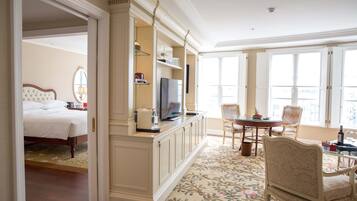 A hotel room with a bed, a TV on a stand, a dining table with chairs, and a large window with shutters.