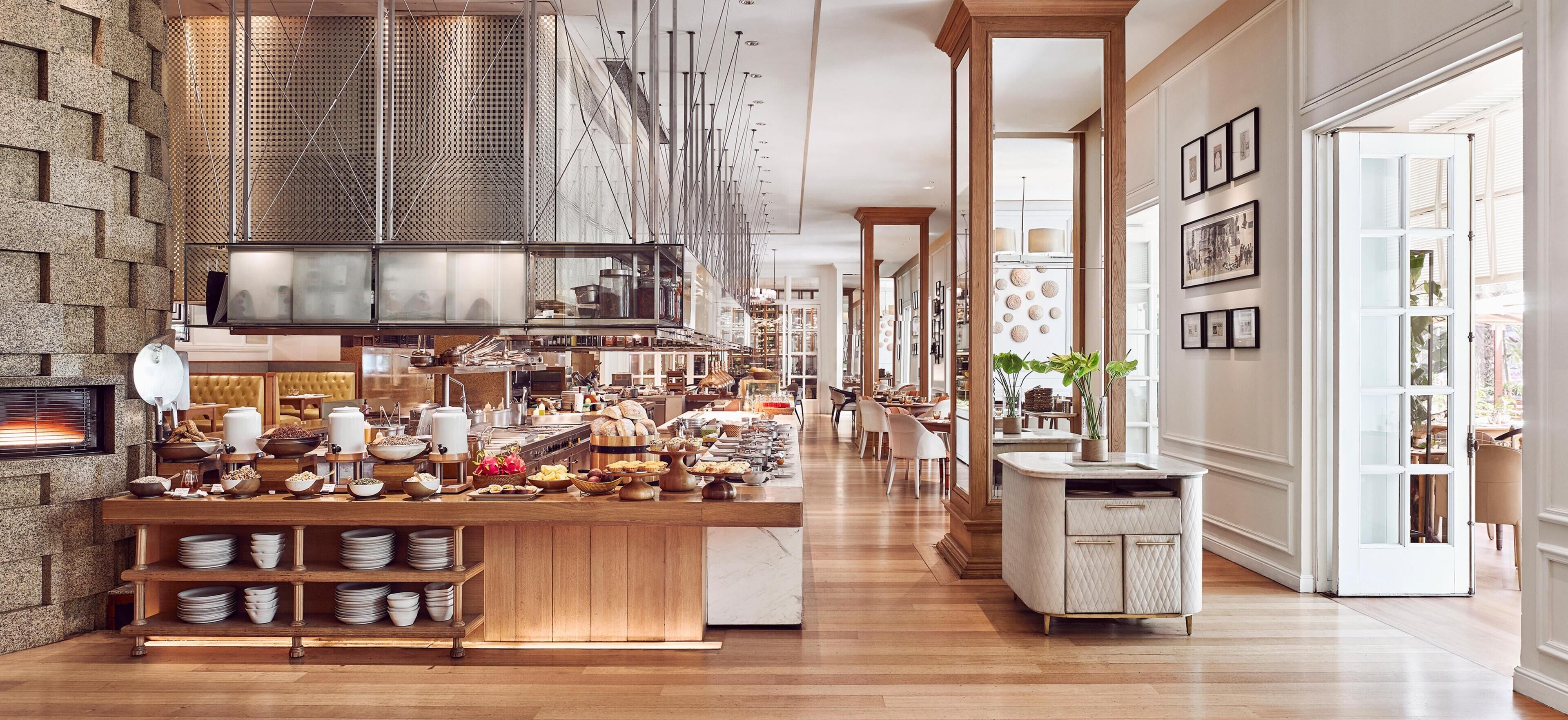 Un hall d’hôtel spacieux avec un comptoir d’accueil central, un mur en pierre et un espace cuisine moderne visible à travers une paroi vitrée.