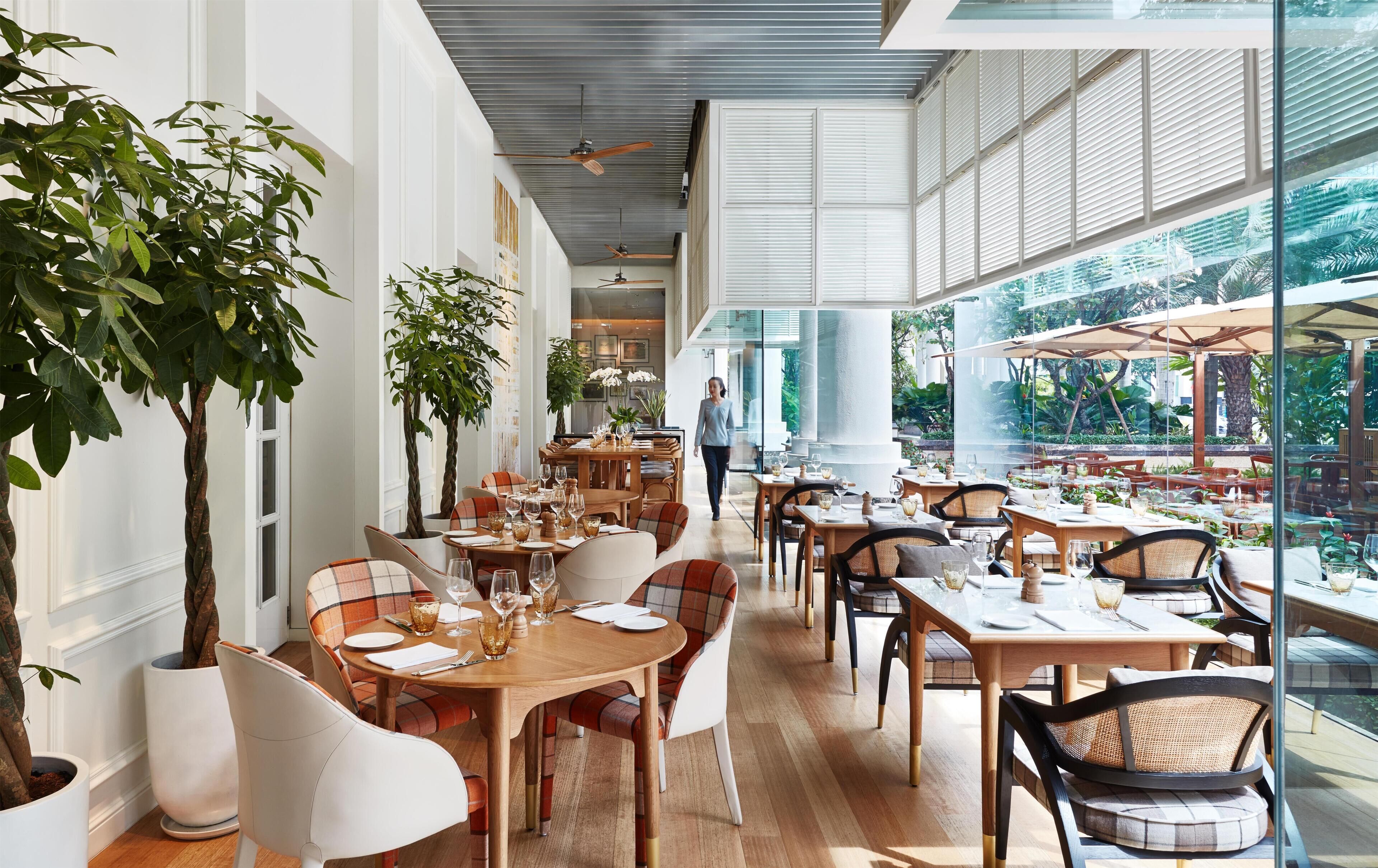 A spacious indoor dining area with high ceilings, large windows, and indoor plants.