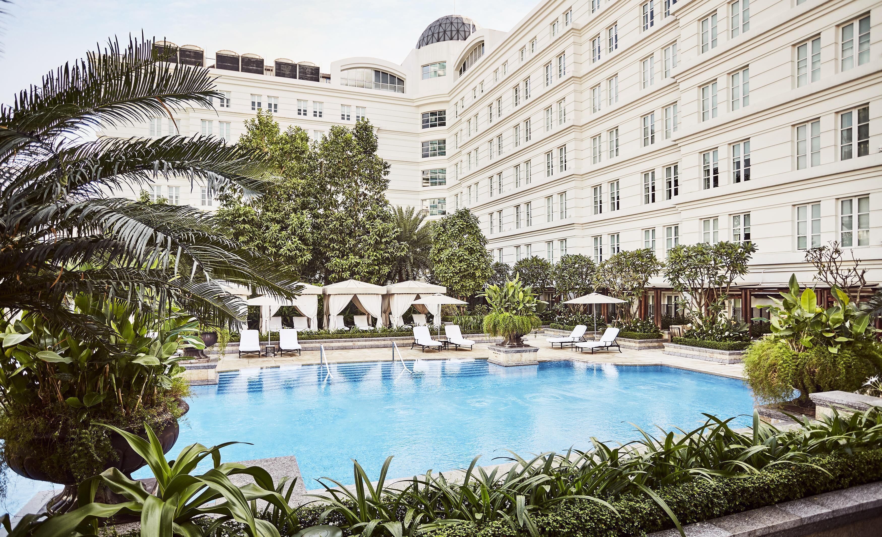 Un hotel con piscina, sillas de descanso y plantas tropicales.