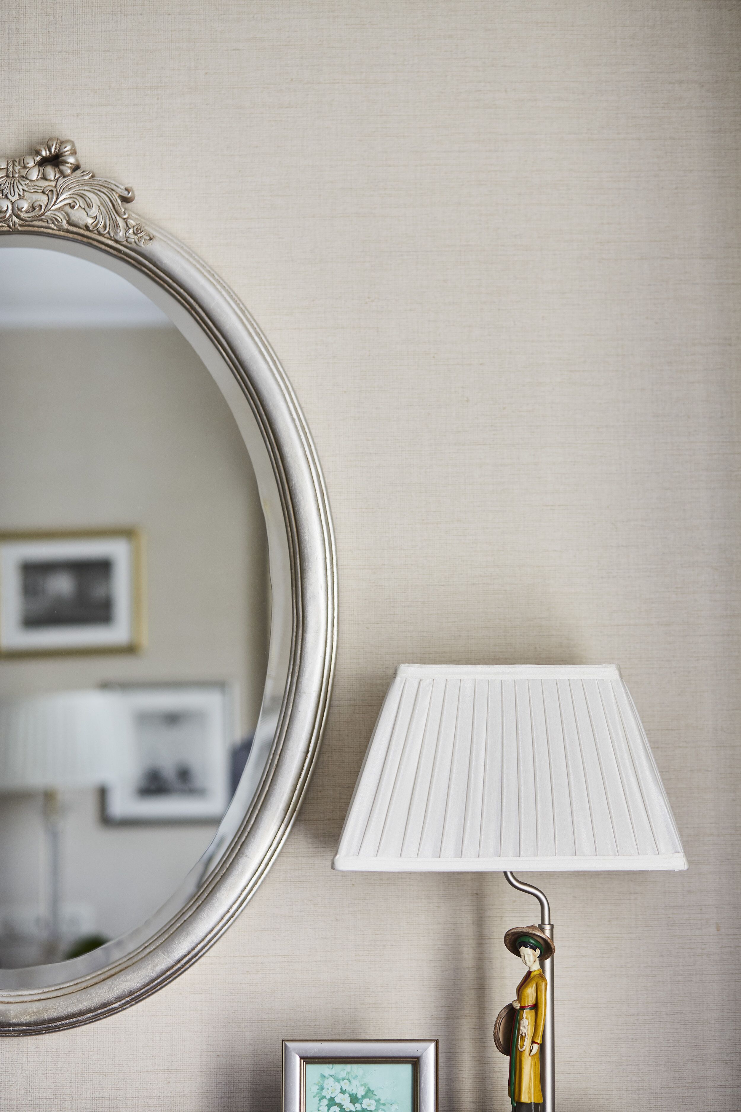 Ein Spiegel mit aufwendigem Rahmen, eine weiße Lampe mit Klappenschirm und ein kleines Bild im Bilderrahmen an der Wand.