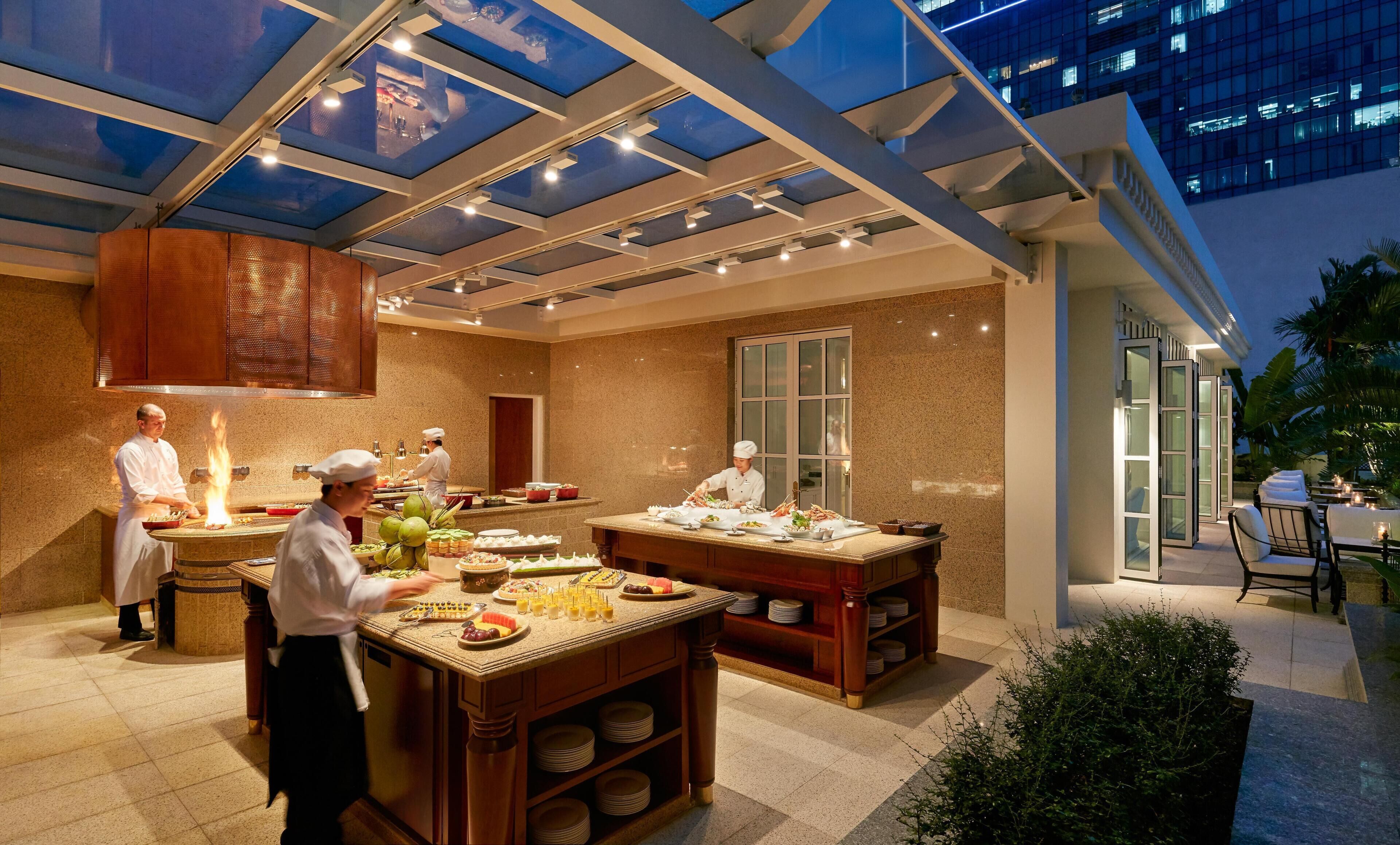 A modern kitchen with chefs preparing food, large windows, and a view of a building.