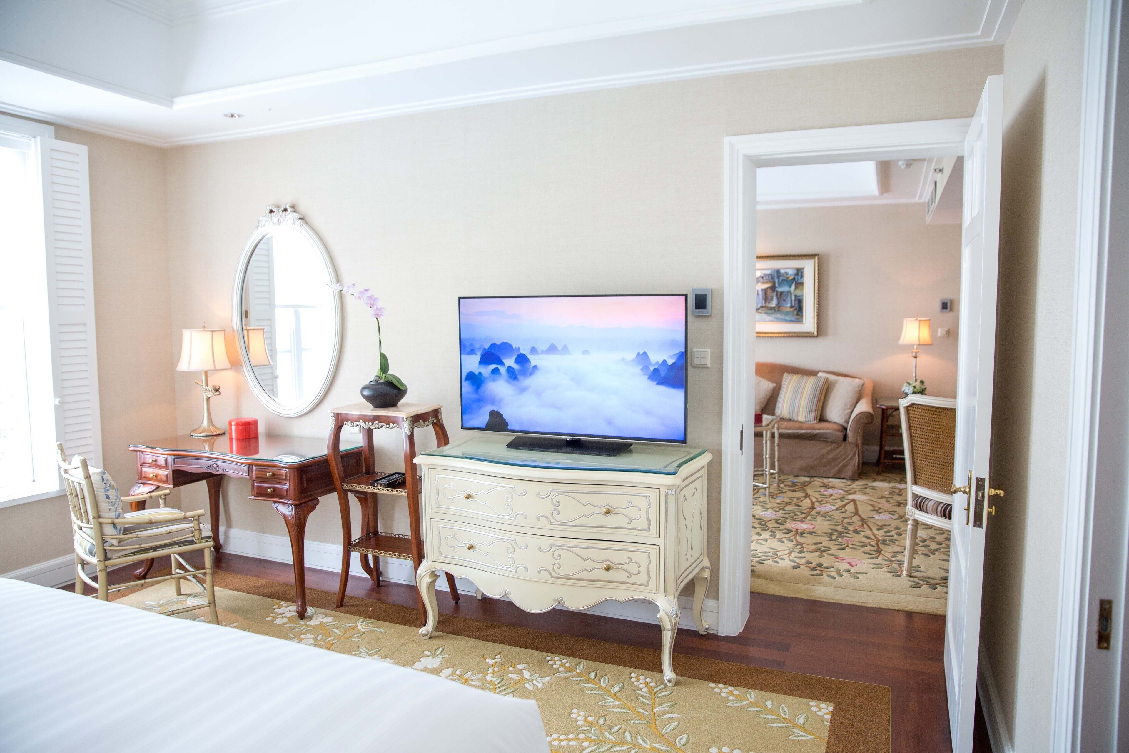 A hotel room with a bed, a desk with a lamp, a television, a dresser, and a chair.