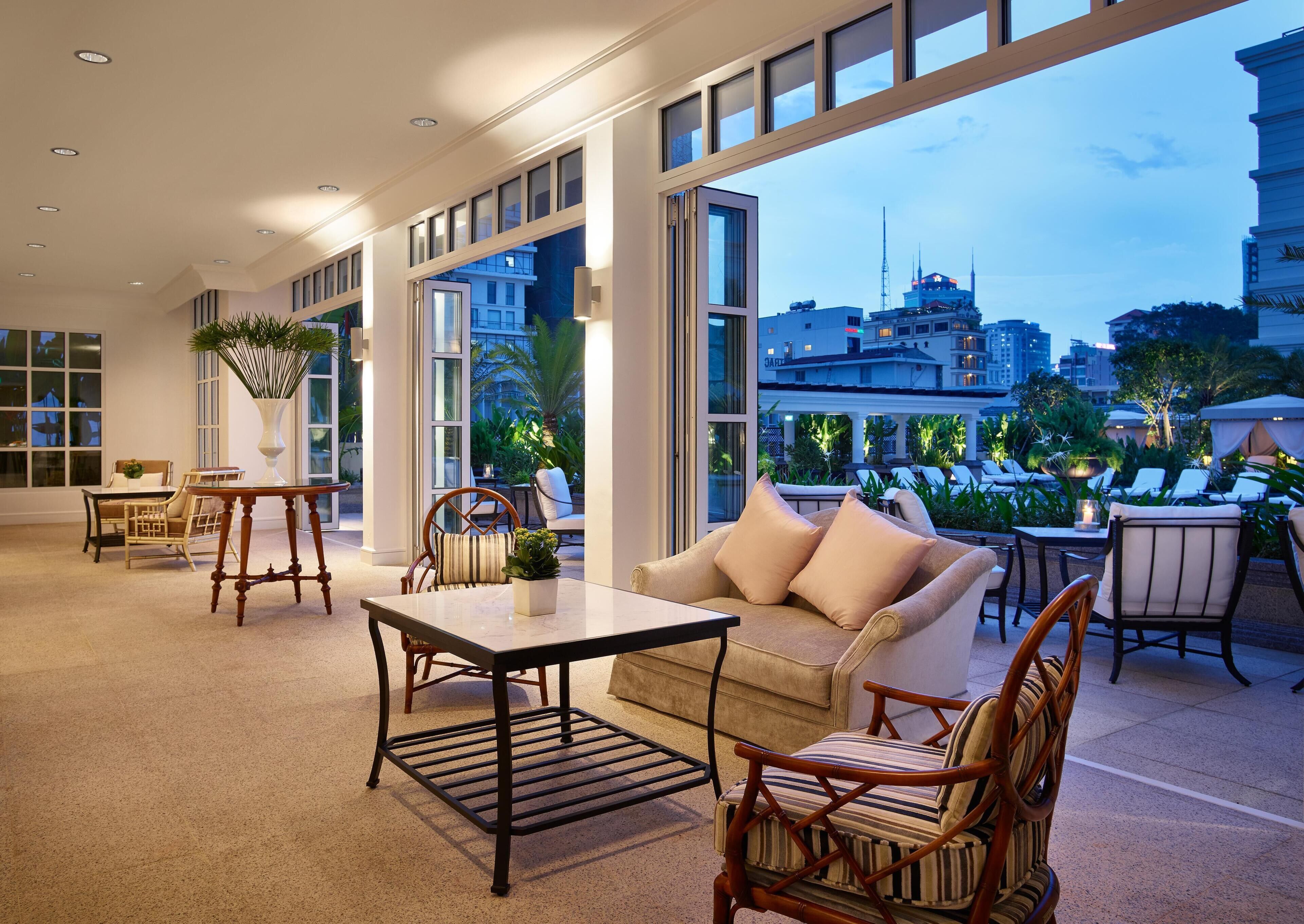 Un interior moderno con un sofá, sillas, una mesa y un amplio ventanal con vista a la ciudad.