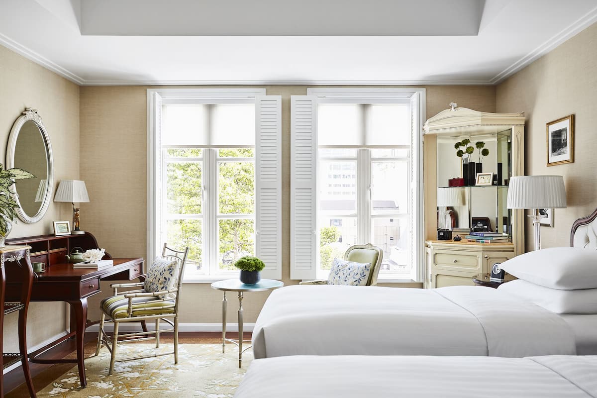 Une chambre d  ’hôtel avec deux lits, un bureau, une chaise, une petite table avec une plante et un grand miroir.