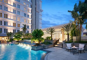 A hotel pool area with a large pool, surrounding greenery, and a modern building in the background.