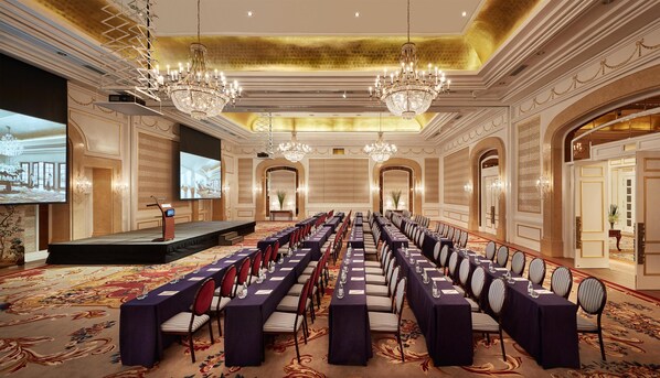 A conference room with a stage, rows of tables, and chandeliers.