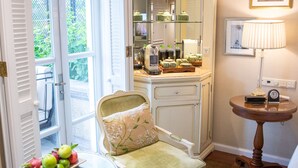 A room with a dining table, a chair, a small round table with a lamp, and a mirror above a counter.