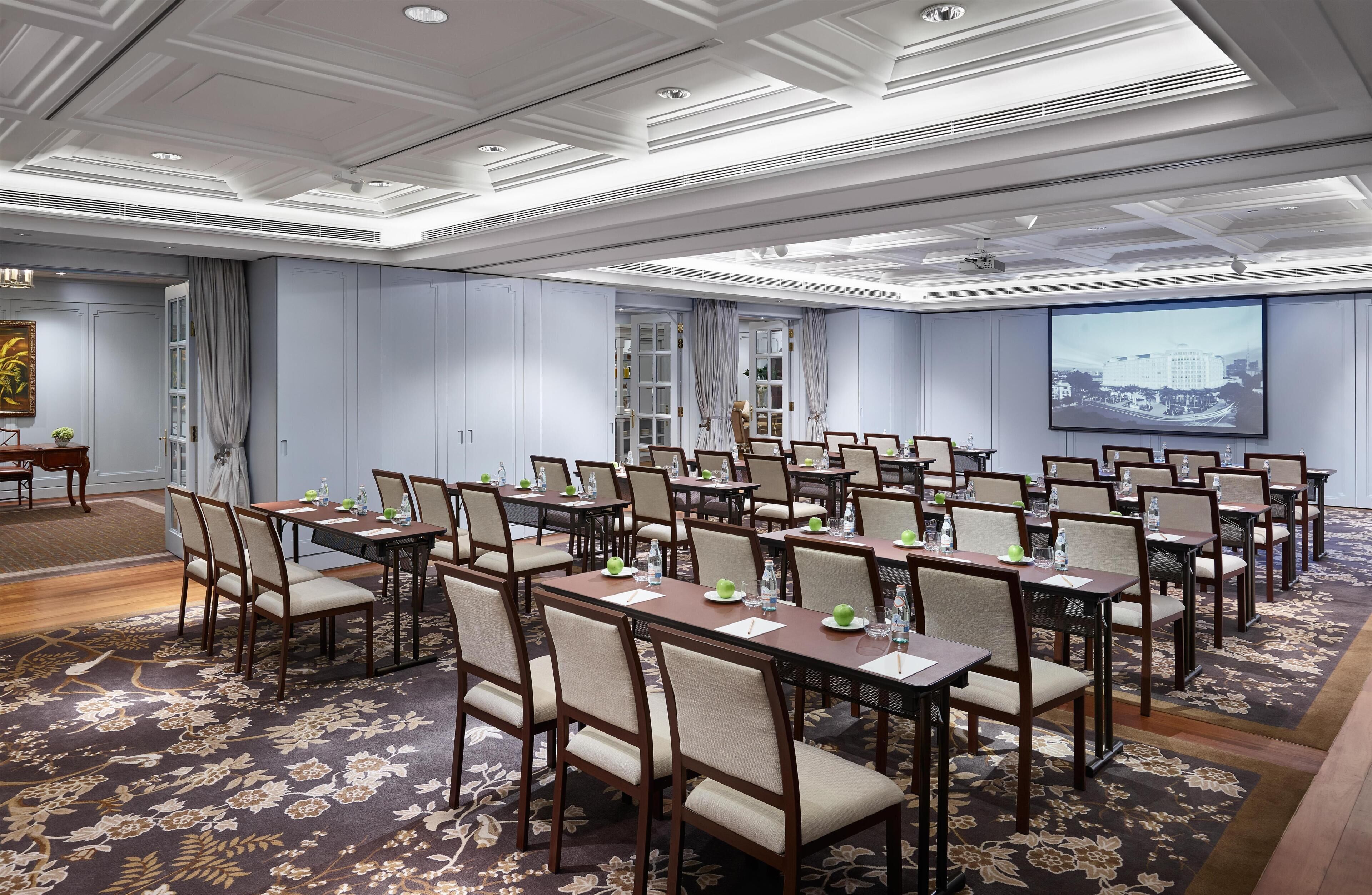 A conference room with multiple tables and chairs, a large screen, and a floral carpet.