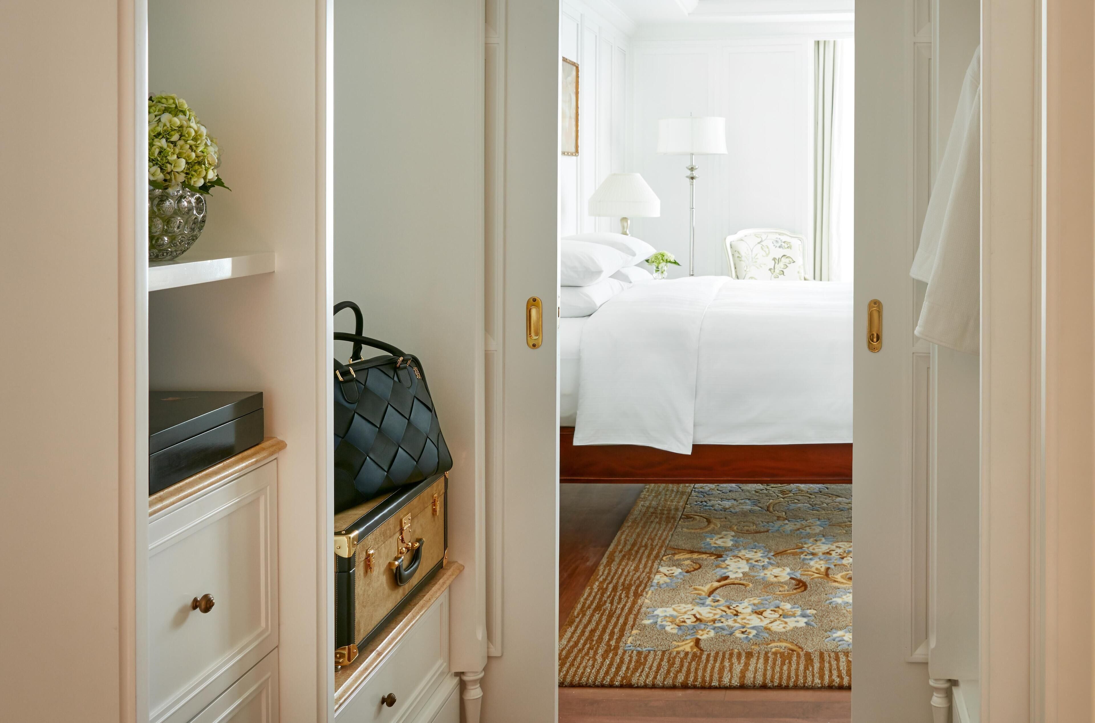 Une chambre d’hôtel avec un lit, une table de chevet, une lampe, une commode et une valise.