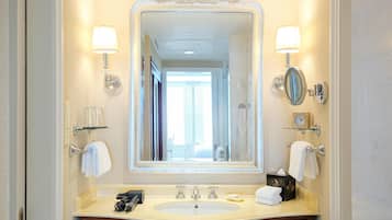 A bathroom with a large mirror, two wall-mounted lamps, a sink with a vanity, and a clock on the wall.