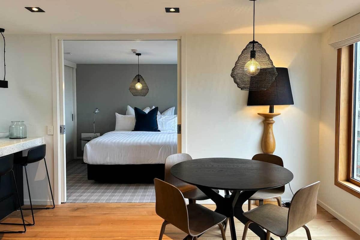 Una habitación de hotel moderna con una cama, un área de comedor con una mesa redonda y sillas, y un pasillo que conduce a otra habitación.