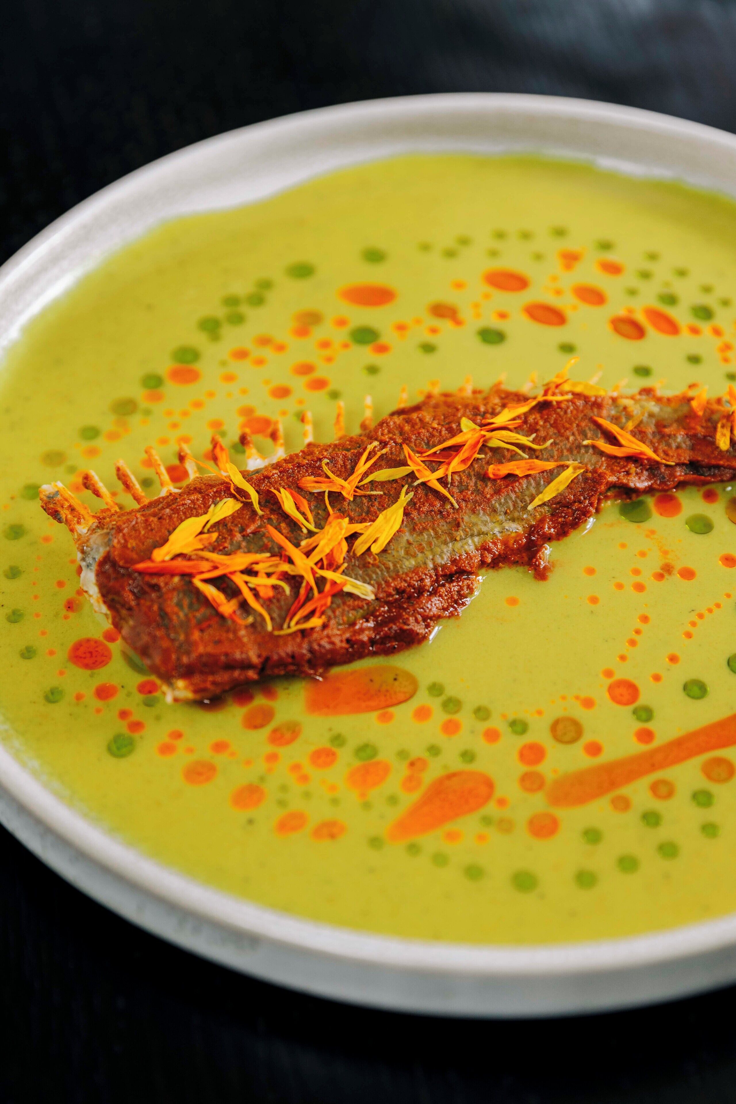 A fish on a green sauce with orange and green dots.